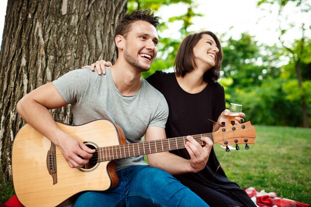 Young beautiful couple smiling, resting on picnic in park.