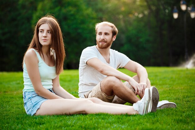 笑みを浮かべて、公園の芝生の上に座っている美しい若いカップル。