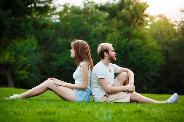 Young beautiful couple smiling, sitting on grass in park.