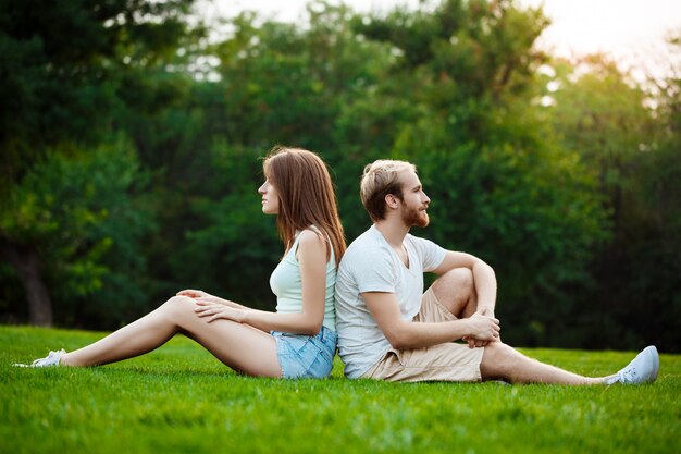 笑みを浮かべて、公園の芝生の上に座っている美しい若いカップル。