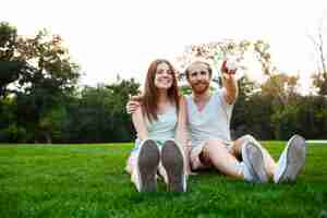 Free photo young beautiful couple smiling, sitting on grass in park.