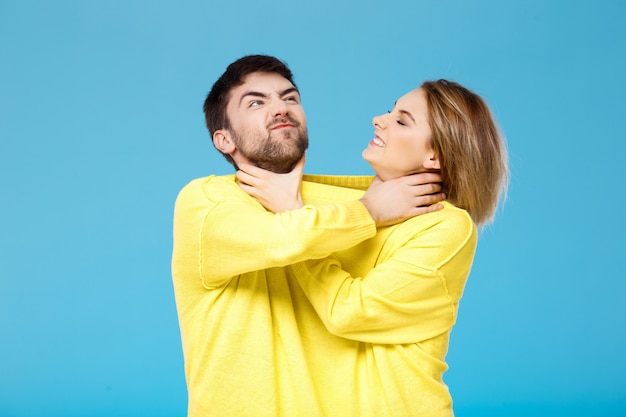 Young beautiful couple smohering each other over blue wall