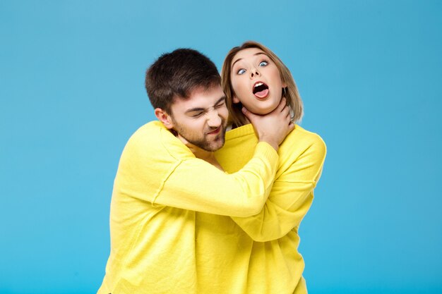 Young beautiful couple smohering each other over blue wall