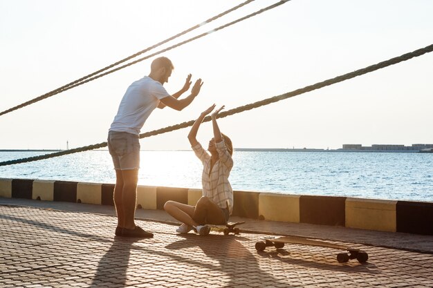 Молодая красивая пара прогулки на берегу моря, давая highfive, скейтбординг.