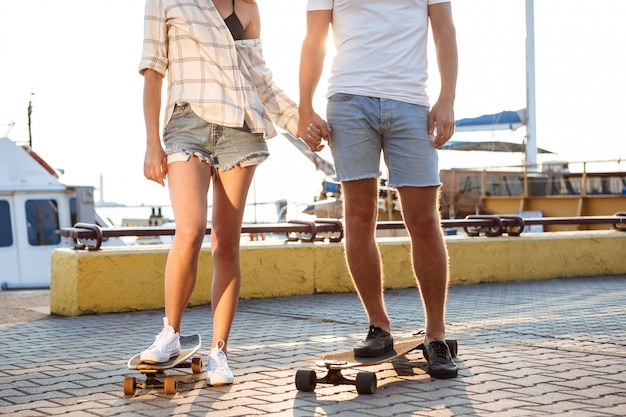 Молодая красивая пара прогулки на берегу моря, скейтбординг. Закройте ноги.