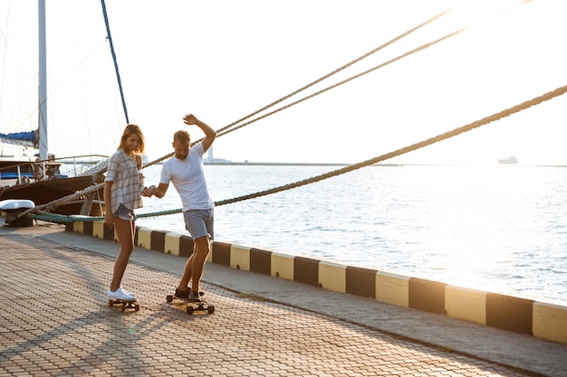 Young beautiful couple walking at seaside, skateboarding.