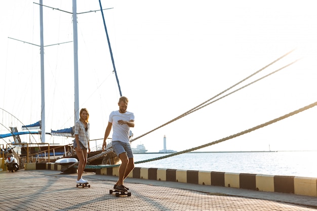 Young beautiful couple walking at seaside, skateboarding.