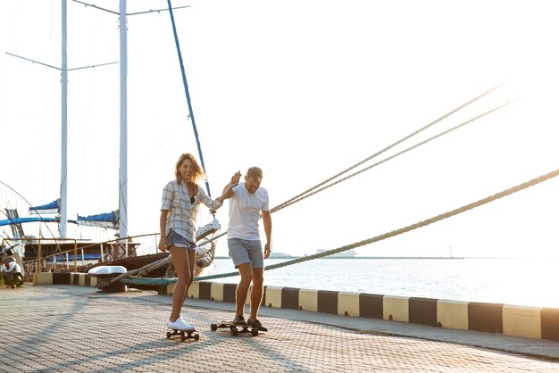 Young beautiful couple walking at seaside skateboarding