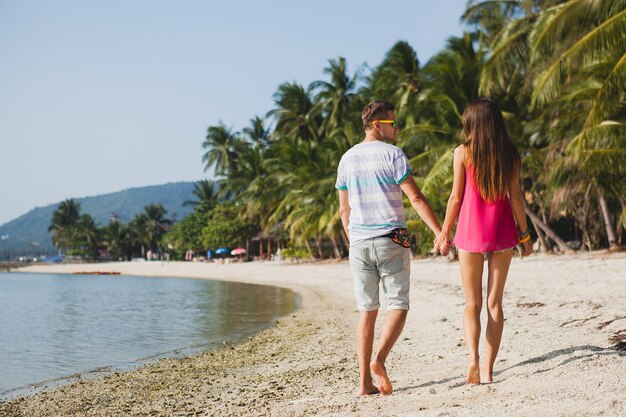 Молодая красивая пара гуляет на тропическом пляже, таиланд, держась за руки, вид со спины, хипстерский наряд, повседневный стиль, медовая луна, отпуск, лето, романтическое настроение, ноги крупным планом, детали