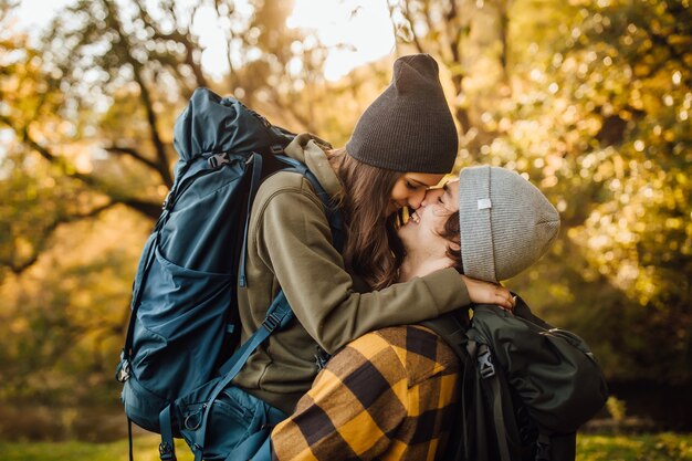 Young beautiful couple with hiking backpack kissing in the forest