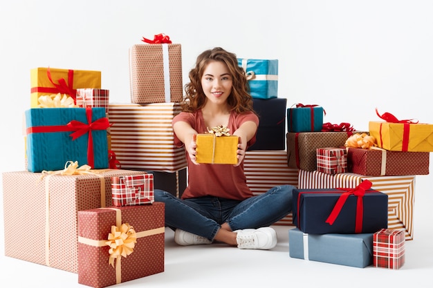 Young beautiful curly girl sitting on floor among gift boxes Isolated