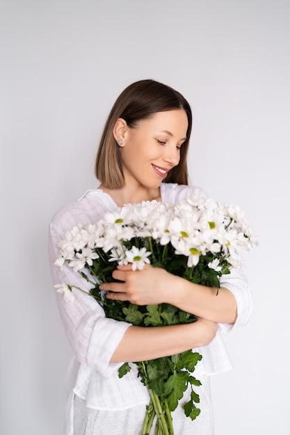 Young beautiful cute sweet lovely smiling woman with hold a bouquet of white fresh flowers on white wall background