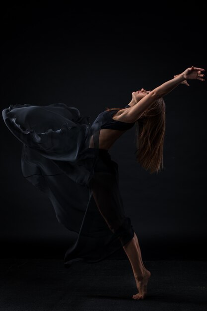 Young beautiful dancer in beige dress dancing on black background