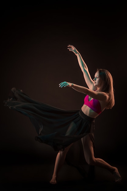 Young beautiful dancer in beige dress dancing on black background