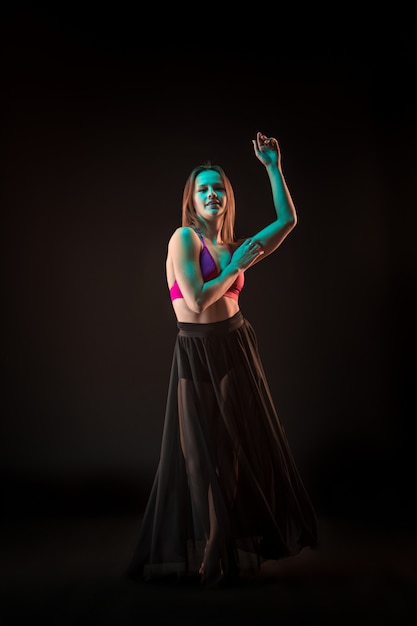 Free photo young beautiful dancer in beige dress dancing on black wall