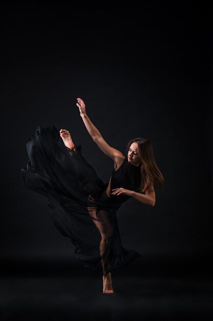 Young beautiful dancer in beige dress dancing on black wall