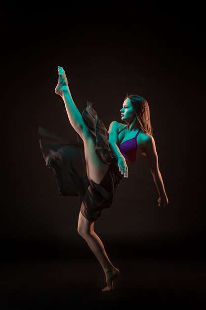 Young beautiful dancer in beige dress dancing on black wall