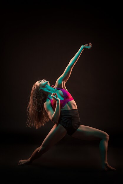 Young beautiful dancer in beige dress dancing on black wall