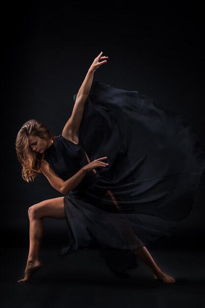 Young beautiful dancer in beige dress dancing on black