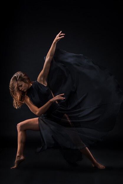 Молодая красивая танцовщица в бежевом платье танцует на черном