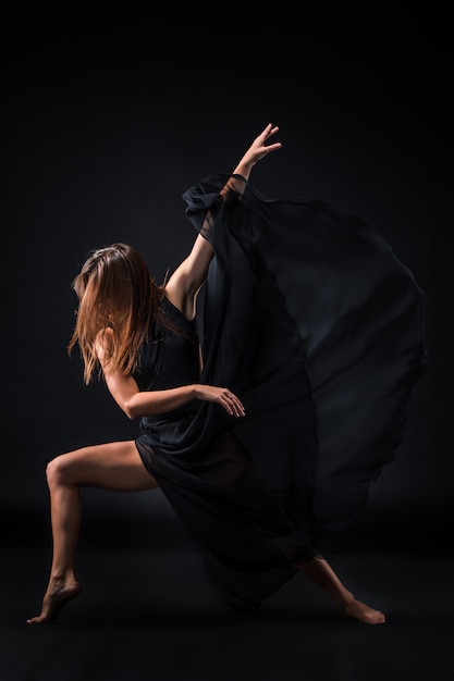 Молодая красивая танцовщица в бежевом платье танцует на черном