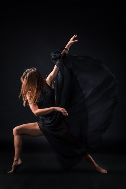 Young beautiful dancer in beige dress dancing on black