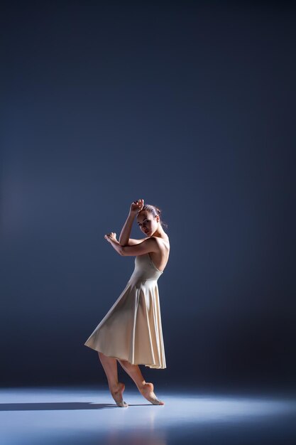 Young beautiful dancer in beige dress dancing on gray