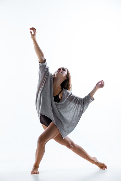 Young beautiful dancer in beige dress dancing on white wall