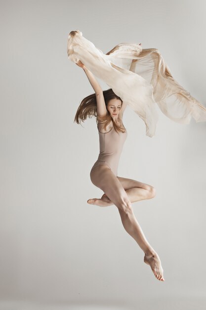 Young beautiful dancer in beige swimsuit dancing on gray