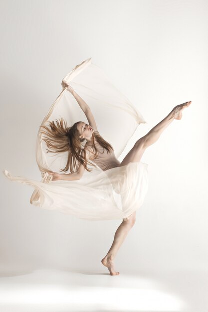 Young beautiful dancer in beige swimsuit dancing on gray