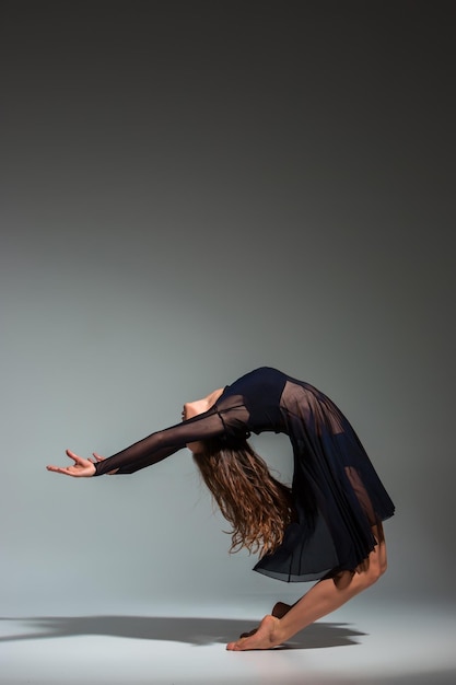 Free photo young beautiful dancer in black dress posing on a dark gray studio background. modern, contemporary, improvisation