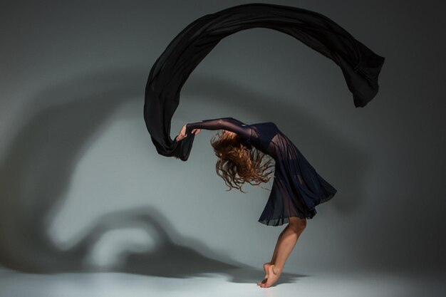 Young beautiful dancer in black dress posing on a dark gray studio background. Modern, Contemporary, improvisation