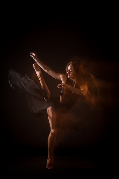 Young beautiful dancer dancing on black wall