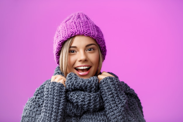 紫に笑みを浮かべてニット帽子とセーターの若い美しい金髪の女性。