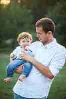 Free photo young beautiful father and little toddler son against green grass