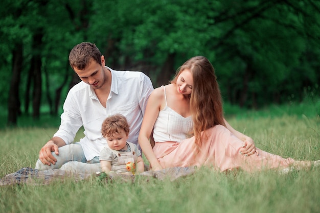 Young beautiful father, mother and little toddler son against green trees