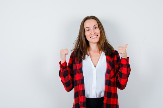 Young beautiful female in casual outfit pointing back with thumbs and looking glad , front view.