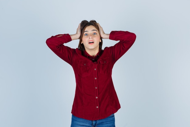 Young beautiful female holding hands on head in shirt and looking troubled