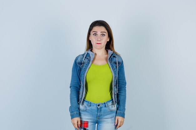 Young beautiful female looking at front in denim outfit and looking bewildered , front view.