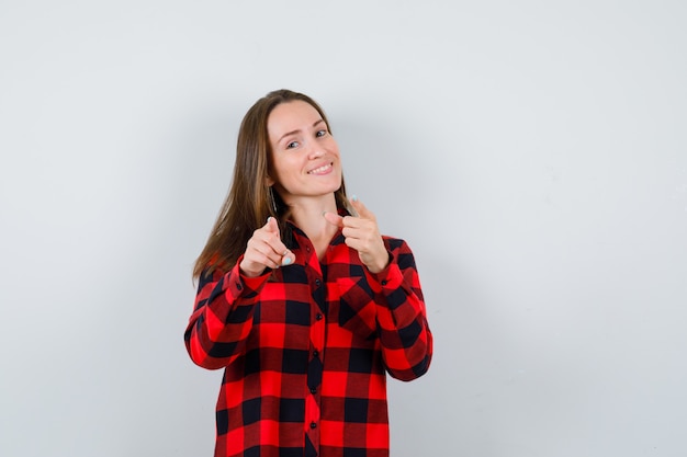 Giovane bella femmina che indica davanti in camicia casual e sembra allegra. vista frontale.