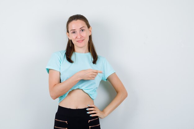 Free photo young beautiful female pointing right in t-shirt and looking blissful , front view.