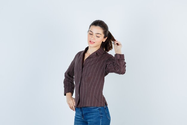 Young beautiful female posing while holding hair with fingers in jacket and looking confident , front view.