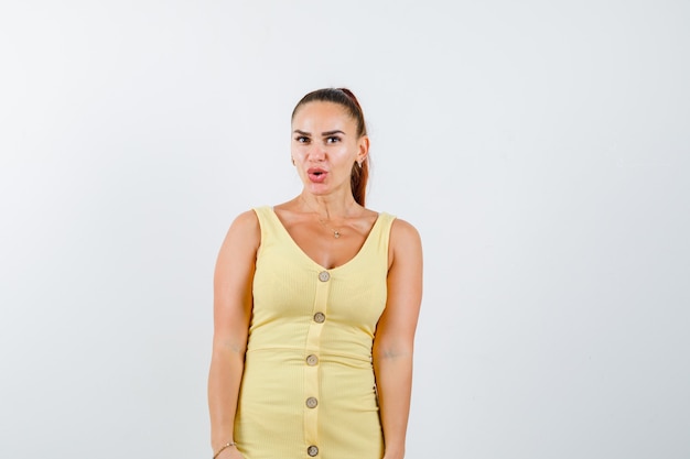 Young beautiful female posing while standing with pouted lips in dress and looking suprised. front view.