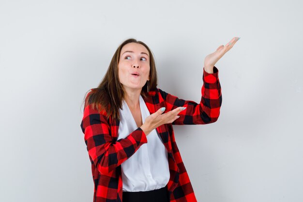 Young beautiful female pretending to show something, looking away in casual outfit and looking joyful. front view.