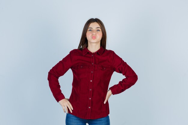 Young beautiful female in shirt posing while holding hands on waist and looking cheerless