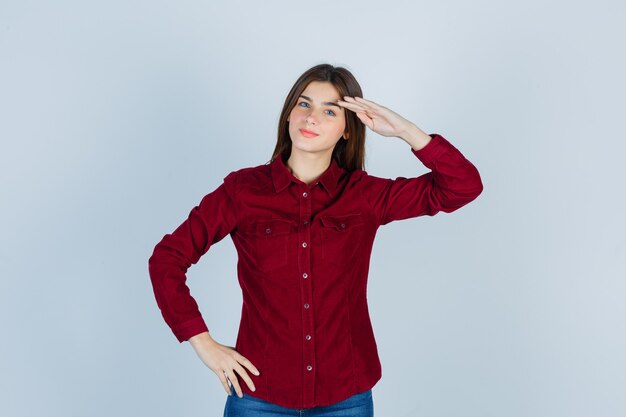 Young beautiful female showing salute gesture in shirt and looking blissful.