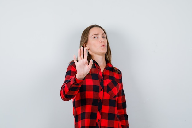 Young beautiful female showing stop gesture in casual shirt and looking confident. front view.