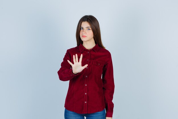 Young beautiful female showing stop gesture in shirt and looking cheerless.