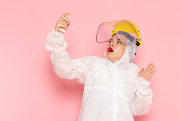 young beautiful female in special white suit and helmet using spray on pink