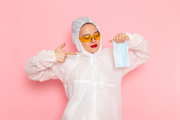 young beautiful female in special white suit holding sterile mask on pink